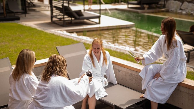 Kurzurlaub in Tirol: Wellness-Auszeit im ADEA Fieberbrunn Vier Frauen in Bademänteln entspannen am Pool und stoßen mit Getränken an