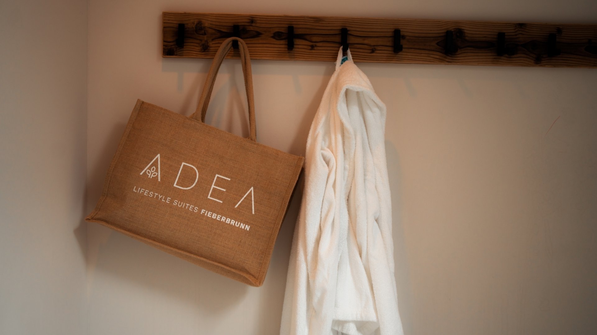 Day Spa inmitten der Kitzbüheler Alpen Braune Tasche und weißer Bademantel hängen an Haken an Holzwand