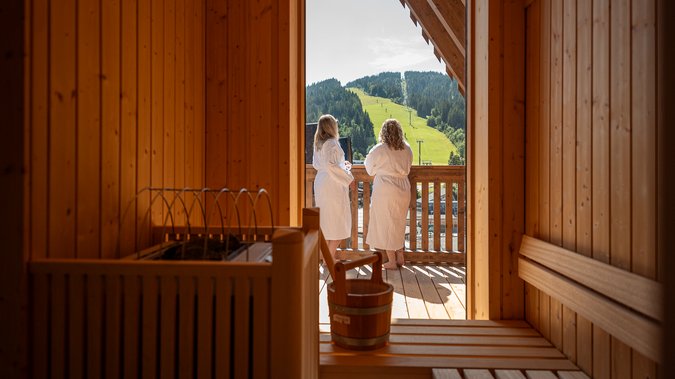 Mit Freundinnen in den Urlaub in Österreich Zwei Frauen in Bademänteln auf einem Balkon mit Bergblick von einer Sauna aus