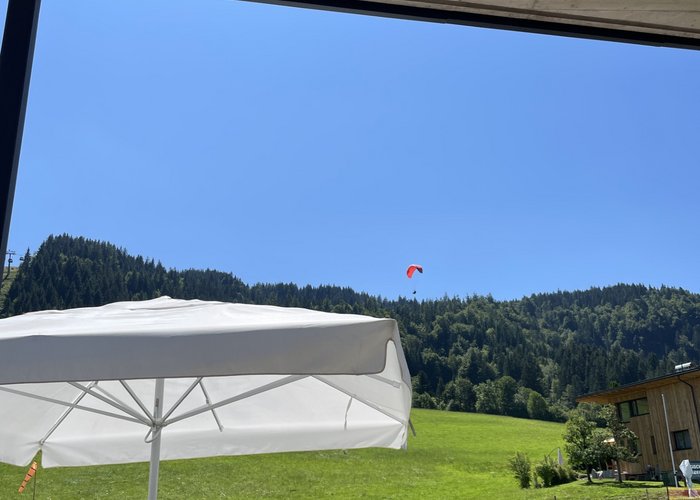 Beim Paragliding Fieberbrunn von oben erleben Person unter weißem Sonnenschirm auf grüner Wiese mit Hügel und Gleitschirm im Hintergrund