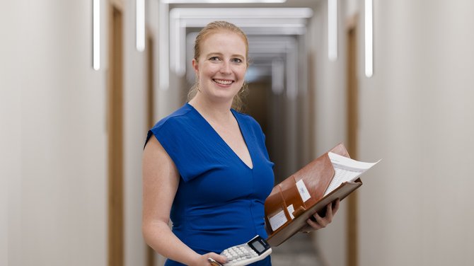 Team der ADEA Lifestyle Suites Fieberbrunn Frau im blauen Kleid mit Taschenrechner und Ordner im Flur