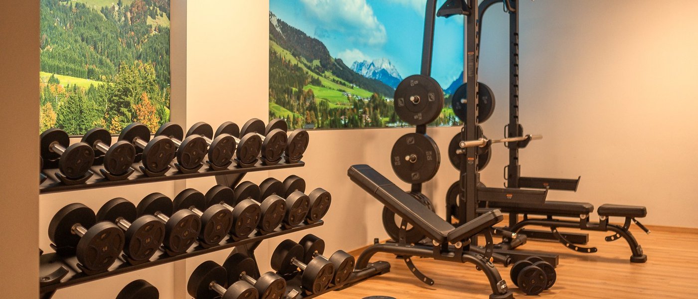Day Spa inmitten der Kitzbüheler Alpen Fitnessraum mit Hanteln und Berglandschaft an der Wand