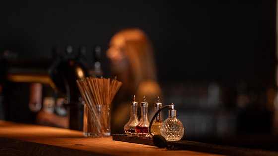 Bar-Equipment steht auf der Bar und im Hintergrund ist verschwommen eine Barkeeperin Bar-Equipment steht auf der Bar und im Hintergrund ist verschwommen eine Barkeeperin