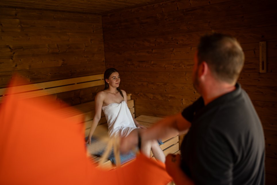 Fieberbrunn: wellness hotel wanted? Woman in white towel sitting in sauna, man performing sauna infusion with towel