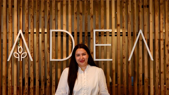 Team der ADEA Lifestyle Suites Fieberbrunn Frau steht vor Holzpaneelen mit dem Schriftzug ADELA
