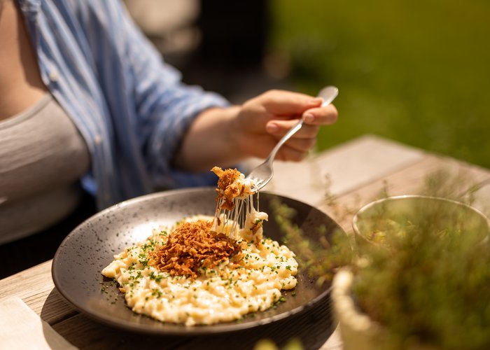 Kulinarische Highlights der Tiroler Küche genießen Person isst cremige Käsespätzle mit Röstzwiebeln im Freien