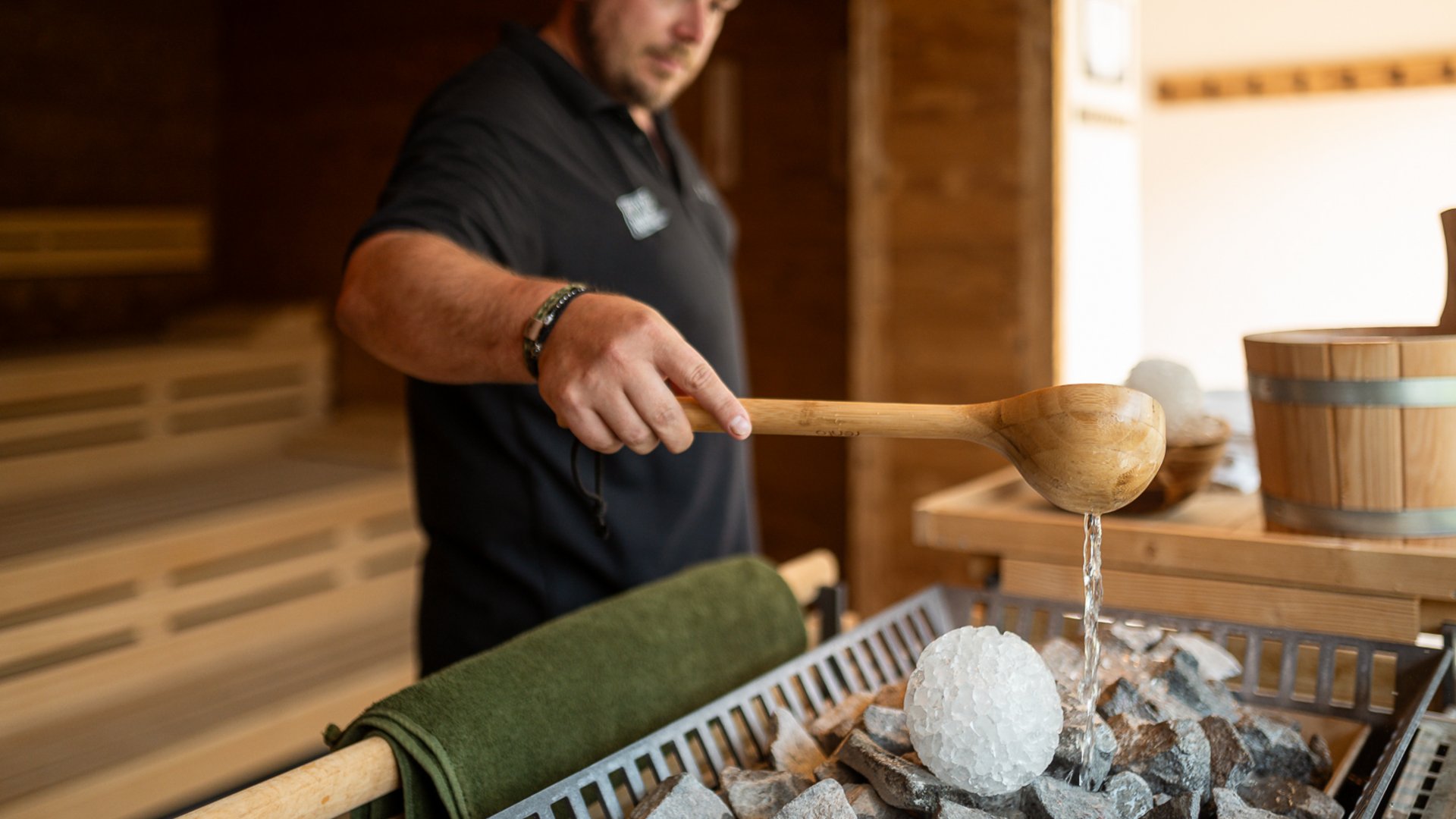 Fieberbrunn: wellness hotel wanted? Man pouring water with ladle on hot stones in sauna