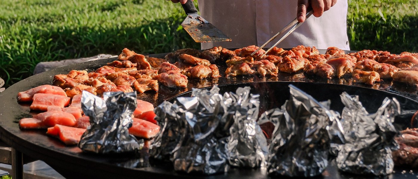 UPSIDEDOWN Restaurant Koch grillt Fleisch und Würstchen auf einer großen Grillplatte im Freien