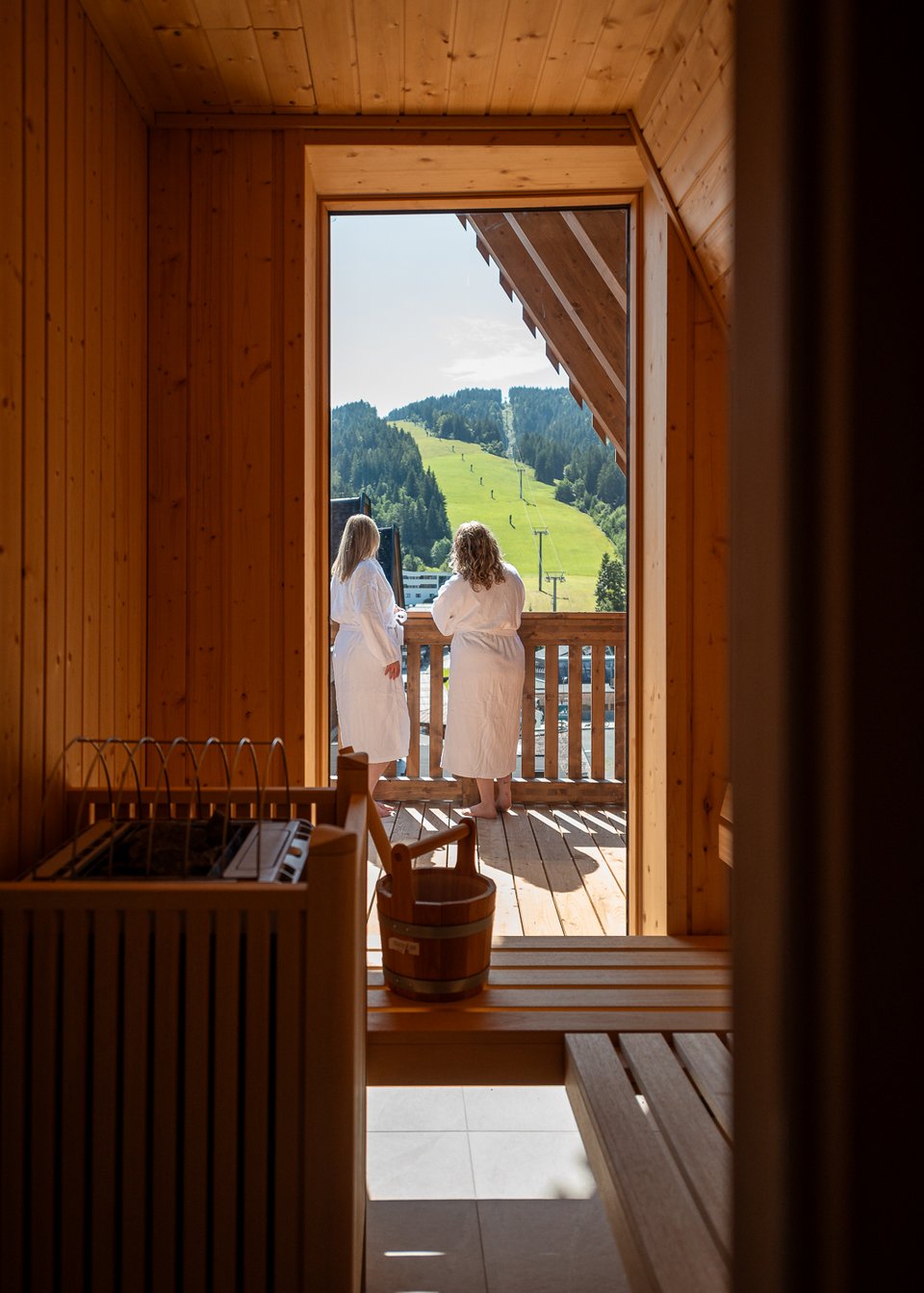 Day Spa inmitten der Kitzbüheler Alpen Zwei Personen in Bademänteln stehen auf Balkon mit Bergblick von Sauna aus.
