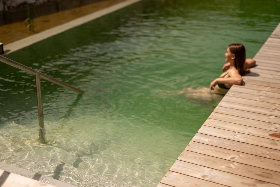 Day Spa inmitten der Kitzbüheler Alpen Frau entspannt im natürlichen Schwimmteich neben Holzdeck
