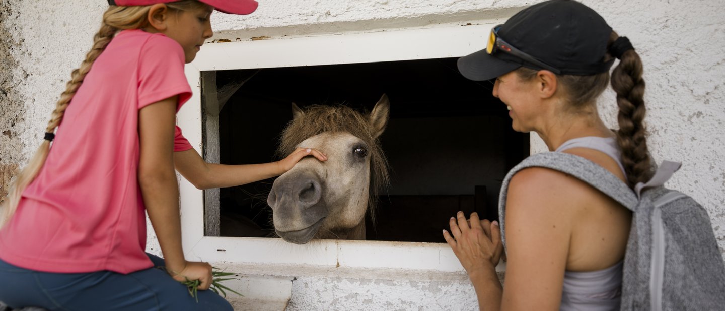 Mutter und Tochter stehen vor dem Stall und streicheln ein Pony Mutter und Tochter stehen vor dem Stall und streicheln ein Pony