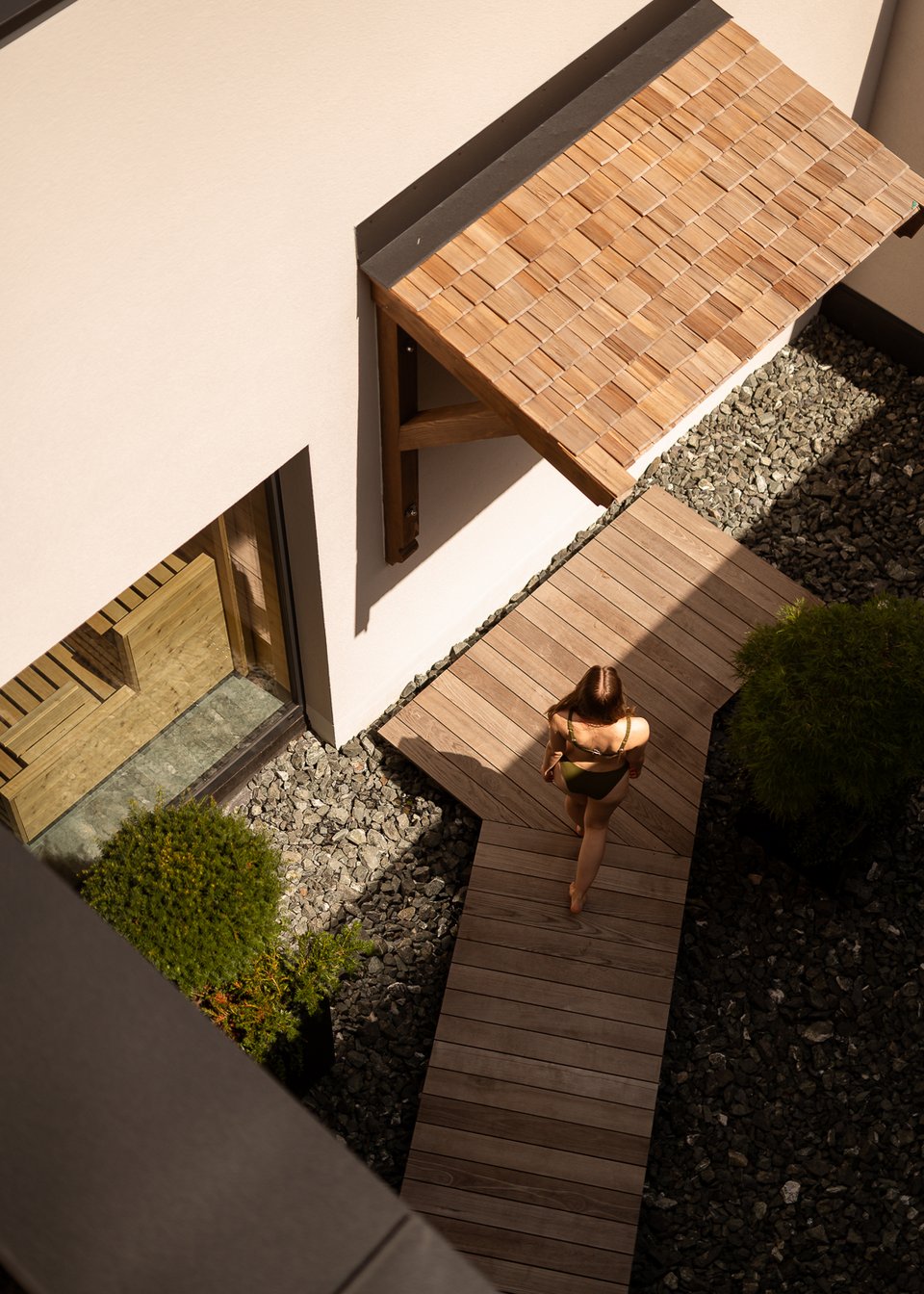 Day Spa inmitten der Kitzbüheler Alpen Frau in Badeanzug geht auf Holzweg neben Steinen und Pflanzen im Innenhof