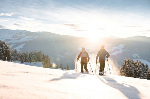 Urlaub für... Zwei Menschen beim Schneeschuhwandern in verschneiter Berglandschaft bei Sonnenuntergang