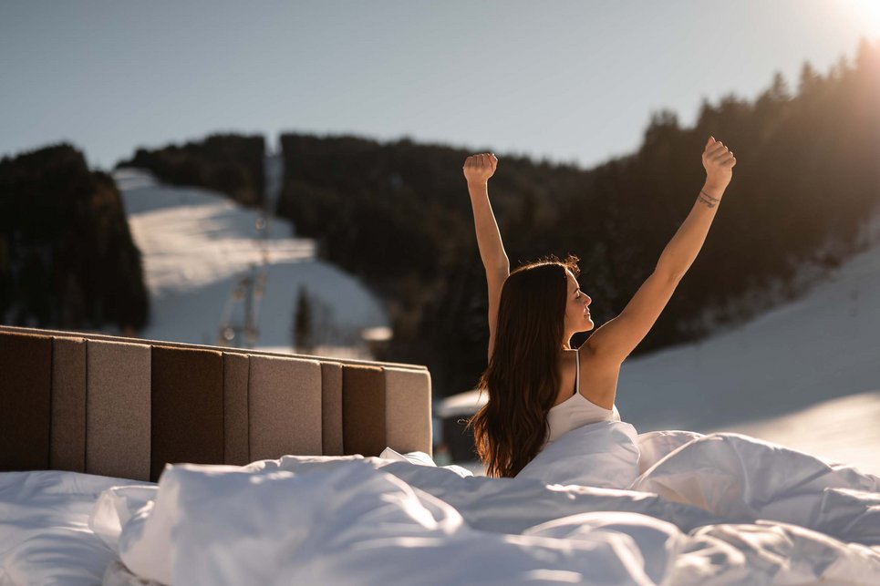 Woman stretches out in bed, which is located directly on the ski slope in Fieberbrunn. Woman stretches out in bed, which is located directly on the ski slope in Fieberbrunn.