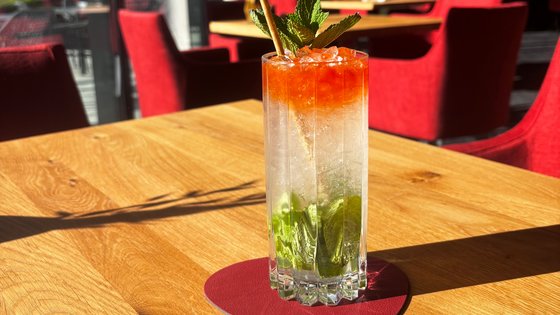 Cocktail mit Minze und Limette auf einem roten Untersetzter auf einem Holztisch Cocktail mit Minze und Limette auf einem roten Untersetzter auf einem Holztisch