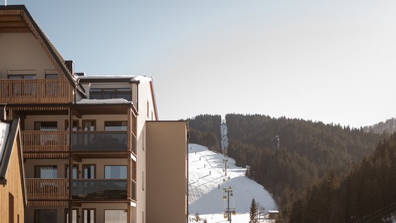 Hotel in Fieberbrunn: ADEA Lifestyle Suites Mehrstöckiges Gebäude mit Balkonen neben einer verschneiten Skipiste und einem Skilift