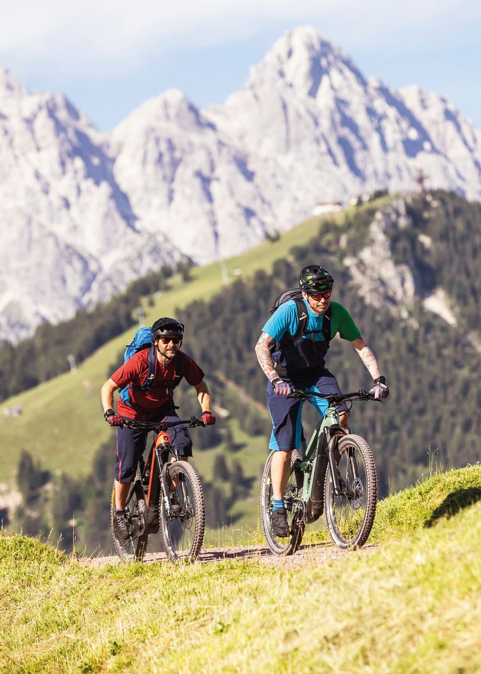 Kurzurlaub in Tirol: Wellness-Auszeit im ADEA Fieberbrunn Zwei Mountainbiker fahren auf einem Bergweg mit Alpen im Hintergrund