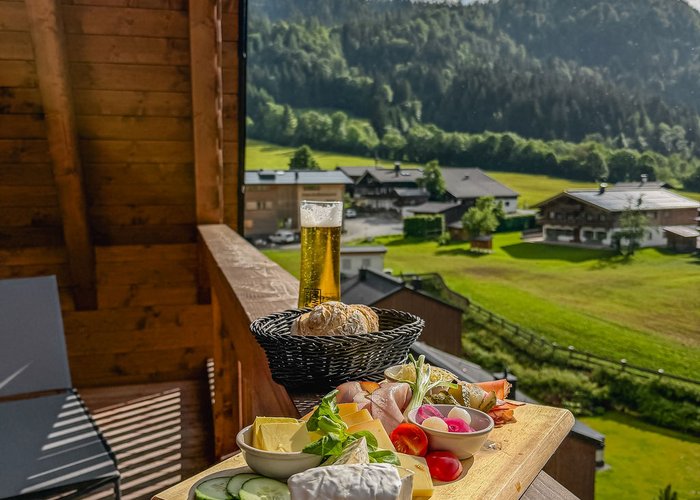 Kulinarische Highlights der Tiroler Küche genießen Brett mit Käse, Gemüse und Brot auf Balkon mit Bergblick bei Sonnenschein