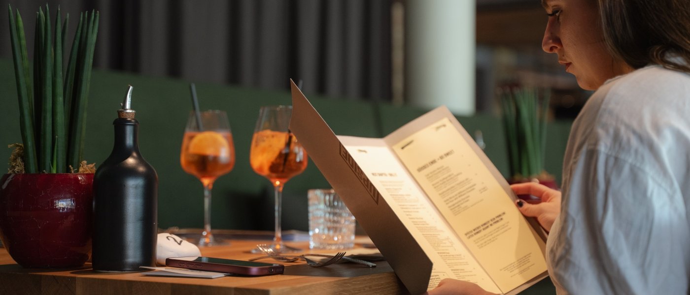 UPSIDEDOWN Restaurant Frau liest in einem Restaurant die Speisekarte an einem gedeckten Tisch