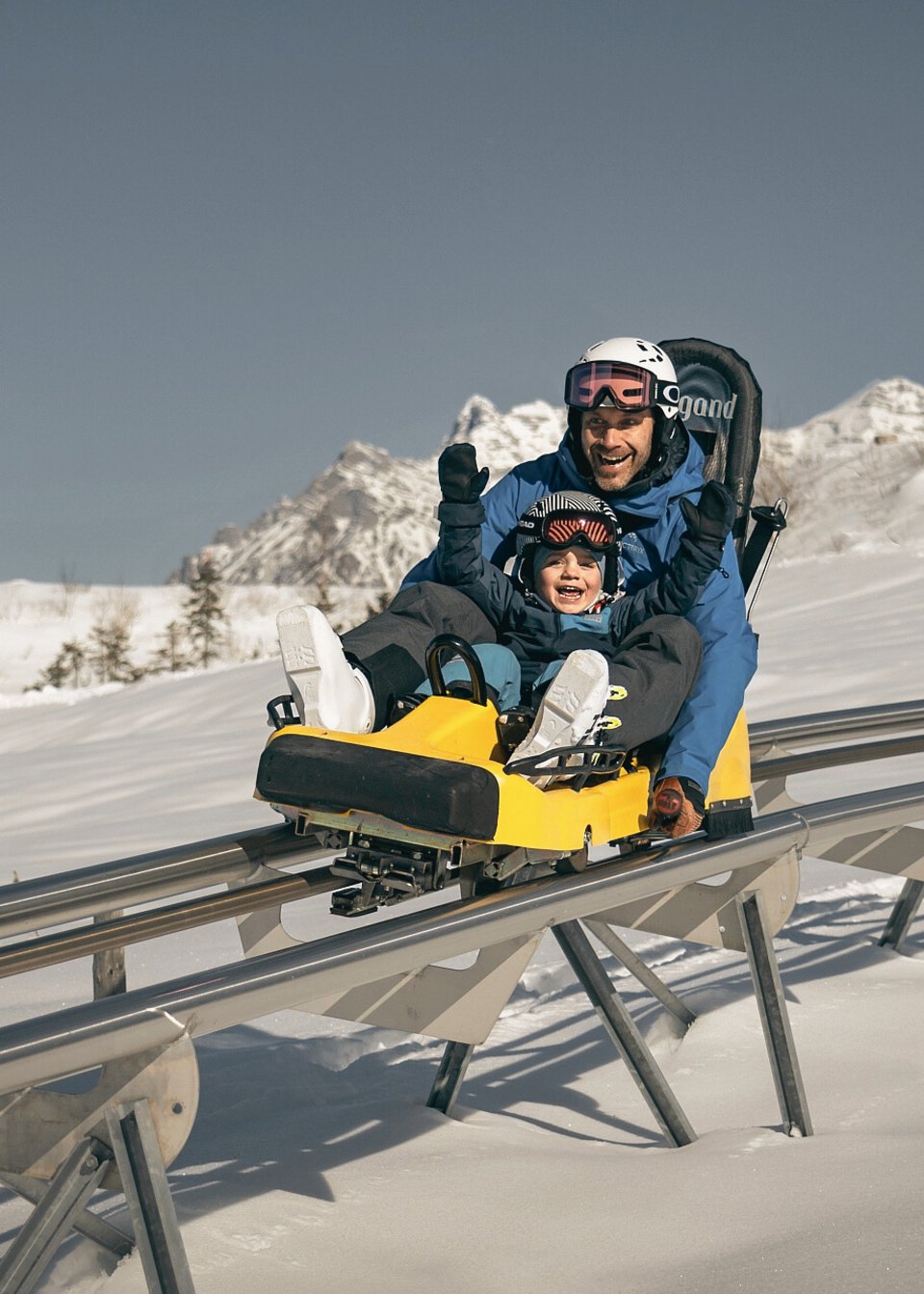 Vater und Kind fahren im Winter auf der Sommerrodelbahn in Fieberbrunn Vater und Kind fahren im Winter auf der Sommerrodelbahn in Fieberbrunn