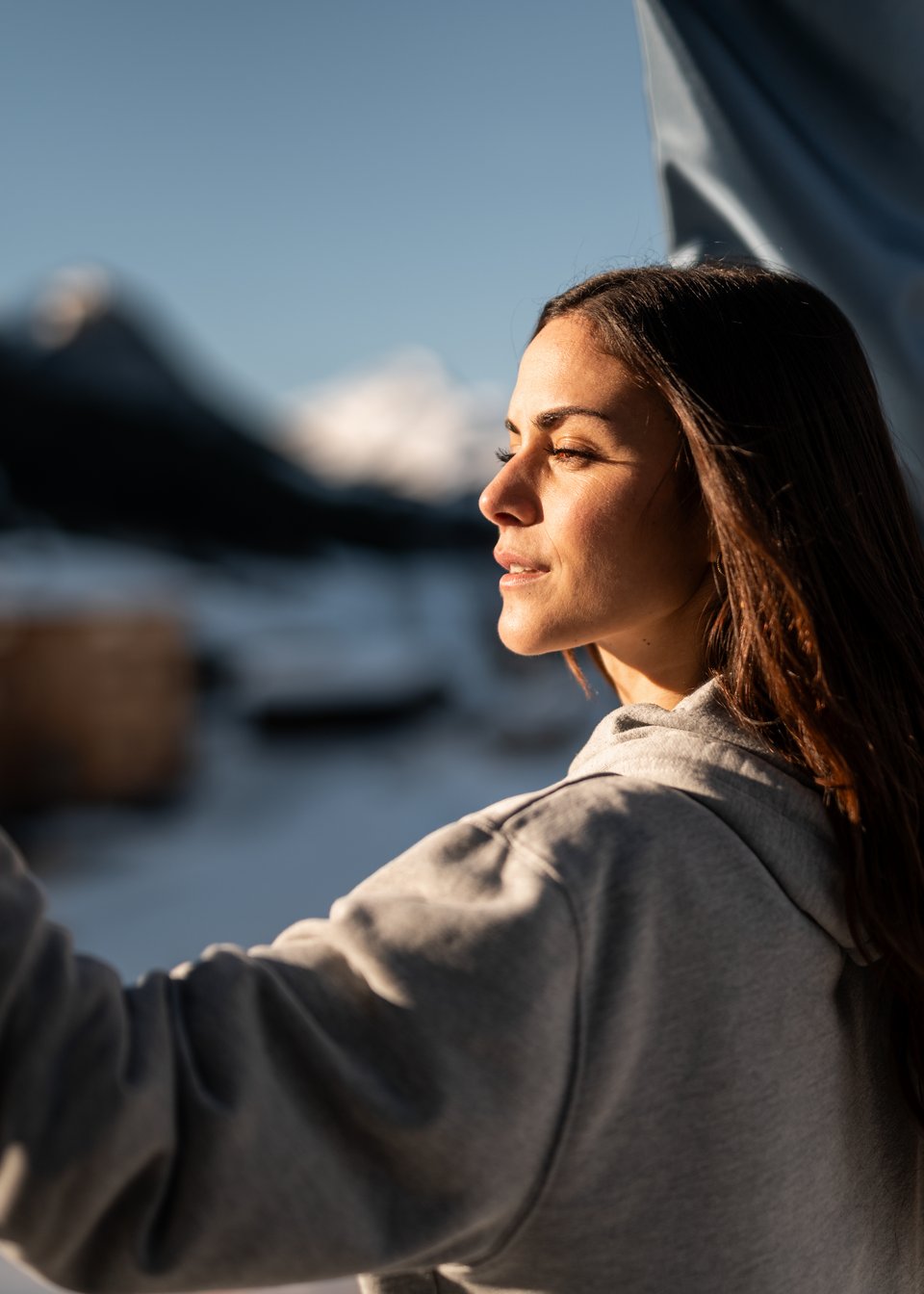 Hotel in Fieberbrunn: ADEA Lifestyle Suites Frau im grauen Hoodie genießt die Sonne mit Berglandschaft im Hintergrund