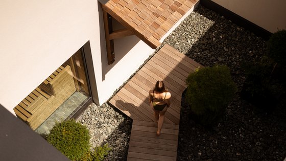 Fieberbrunn: wellness hotel wanted? Woman in swimsuit walking on wooden path surrounded by stones and plants near modern house