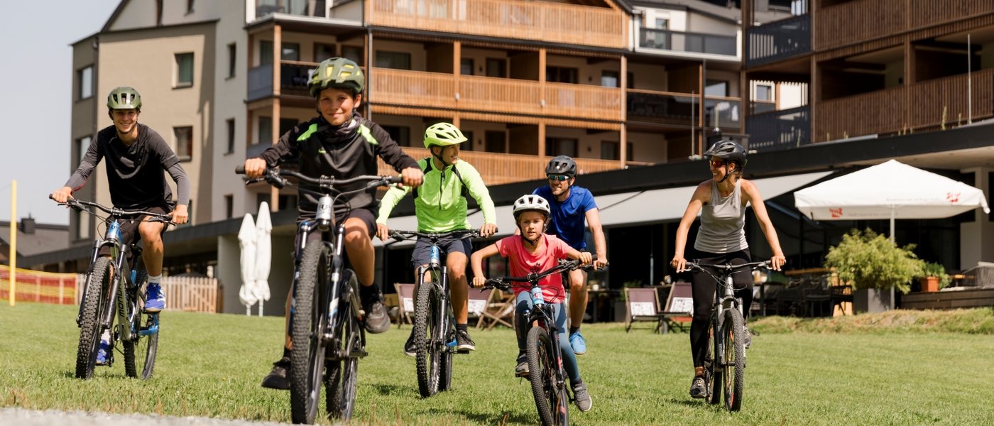 Hotel in Fieberbrunn: the ADEA Lifestyle Suites Family riding mountain bikes together wearing helmets near modern holiday homes