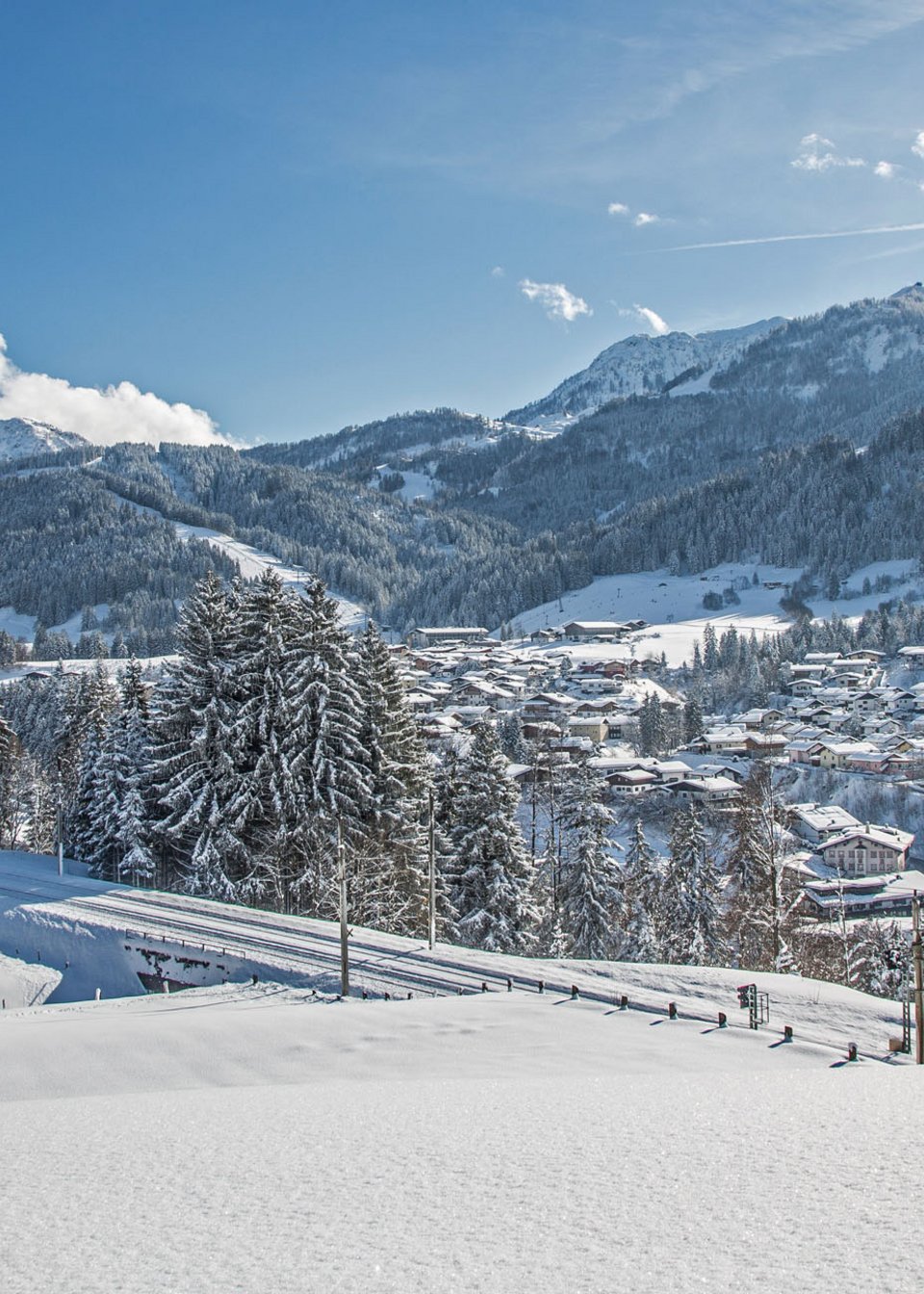 ADEA: dein Hotel mit Fitnessstudio in Österreich Verschneites Dorf mit Kirche in den Alpen unter blauem Himmel