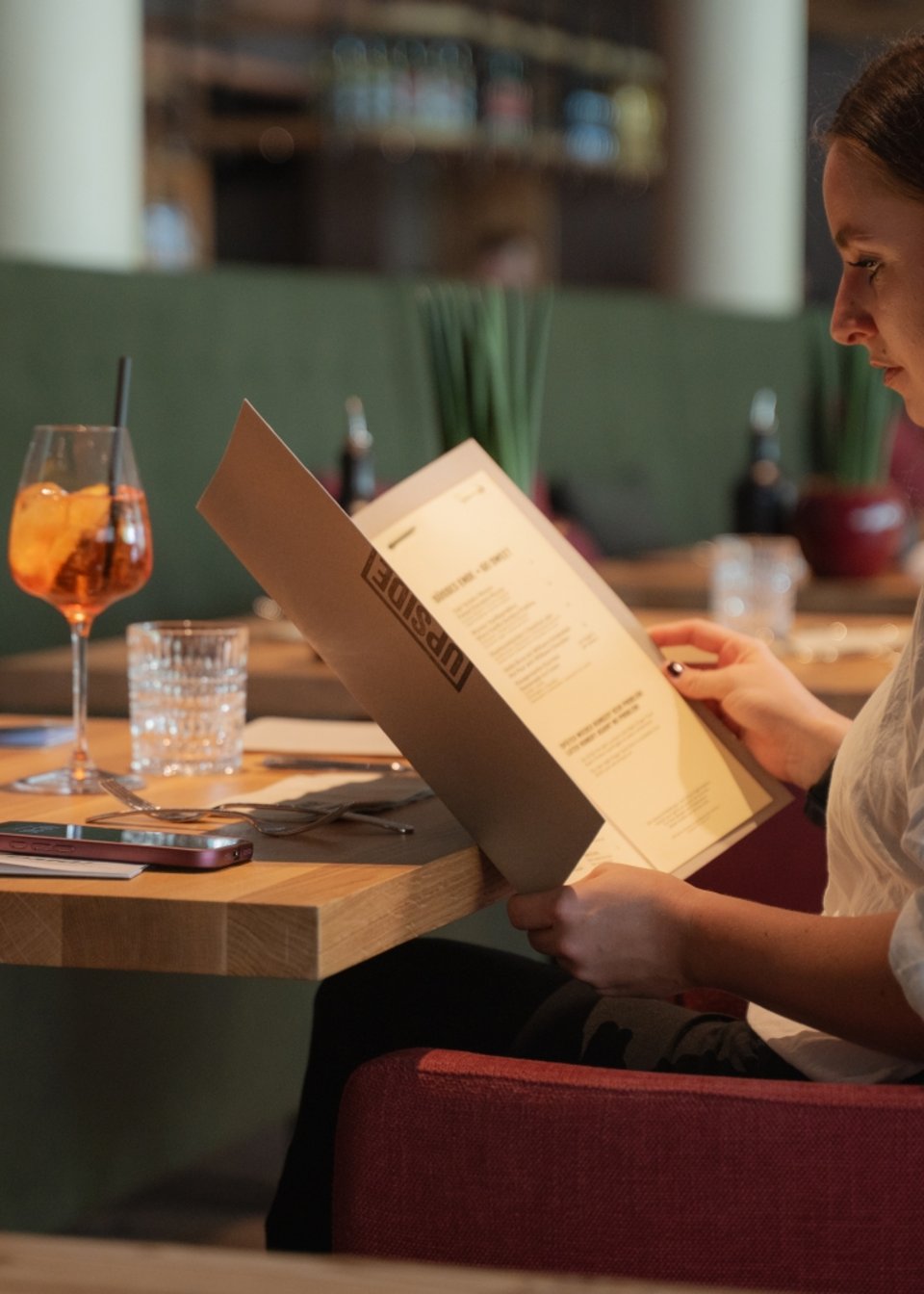 UPSIDEDOWN Restaurant Frau liest in einem Restaurant die Speisekarte am gedeckten Tisch