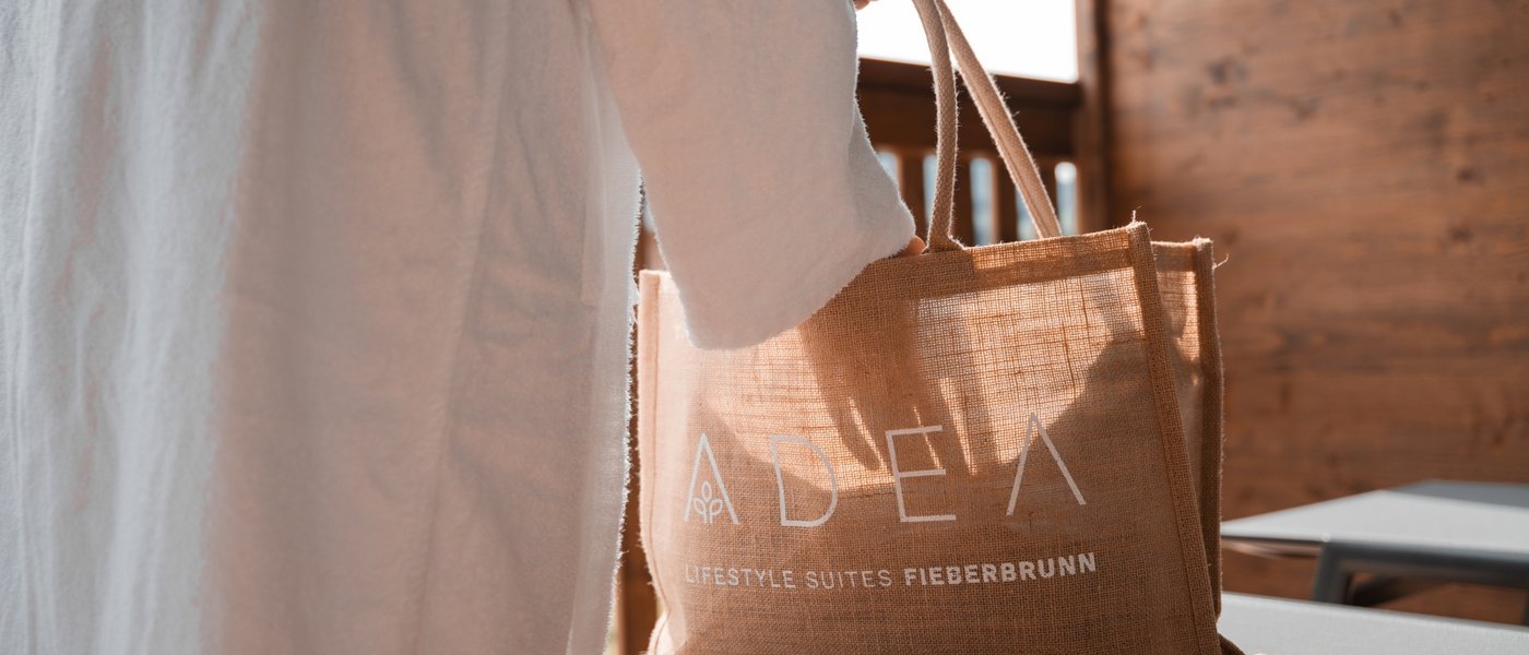 Day Spa inmitten der Kitzbüheler Alpen Hand hält eine Jutetasche mit ADELA Lifestyle Suites Fieberbrunn Aufdruck