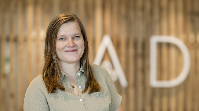 Team der ADEA Lifestyle Suites Fieberbrunn Lächelnde Frau vor verschwommenem Hintergrund mit Buchstaben A und D