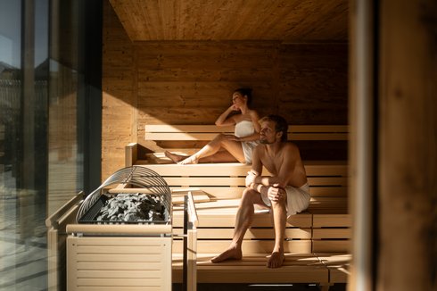 Hotel in Fieberbrunn: ADEA Lifestyle Suites Mann und Frau entspannt in moderner Sauna mit Holzwänden und Ofen