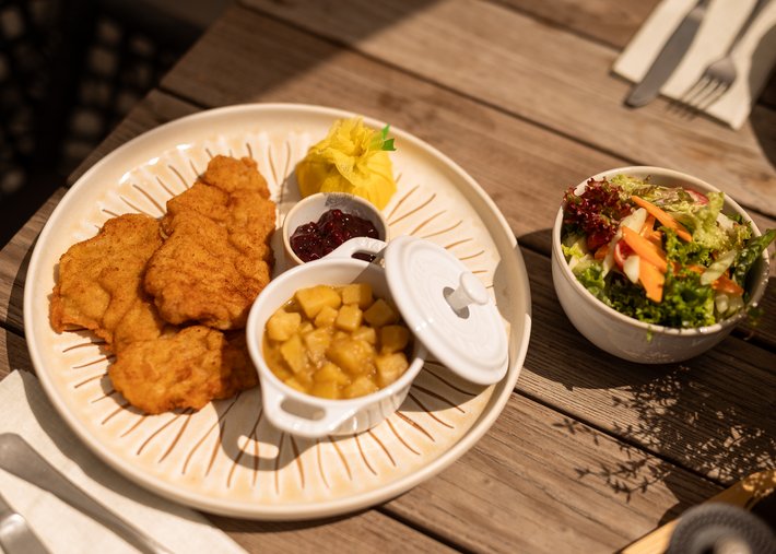 News Teller mit Wiener Schnitzel, Apfelmus, Preiselbeeren und Salat auf Holztisch