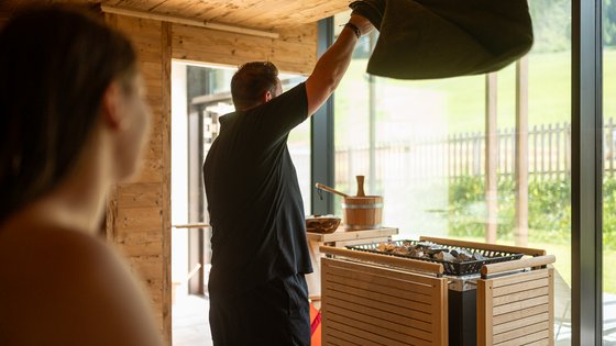 Hotel in Fieberbrunn: ADEA Lifestyle Suites Mann wirft Handtuch in Sauna mit Holzverkleidung und großer Fensterfront
