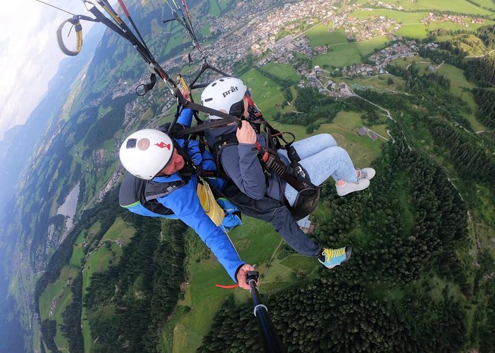News Zwei Personen beim Gleitschirmfliegen über grüne Landschaft und Stadt