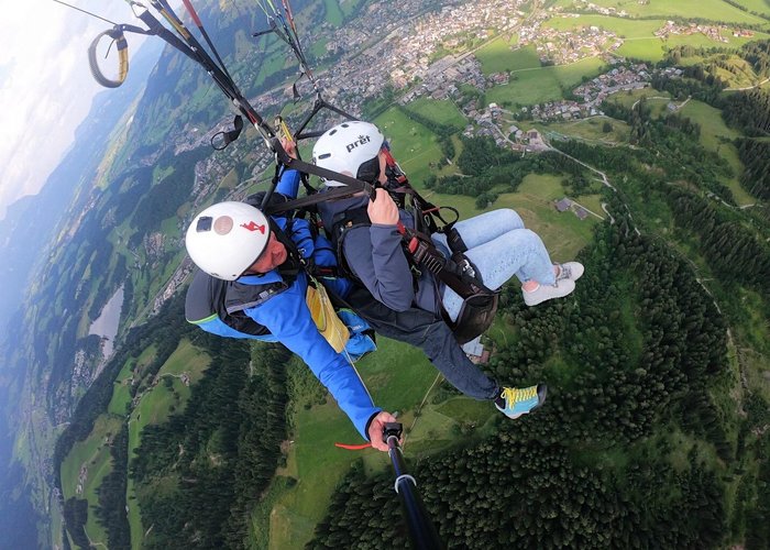 Beim Paragliding Fieberbrunn von oben erleben Zwei Personen beim Gleitschirmfliegen über grüne Landschaft und Stadt