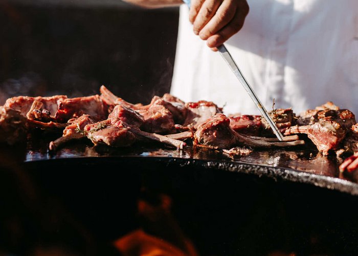 Kulinarische Highlights der Tiroler Küche genießen Person wendet Fleischstücke auf einem Grill mit Grillzange