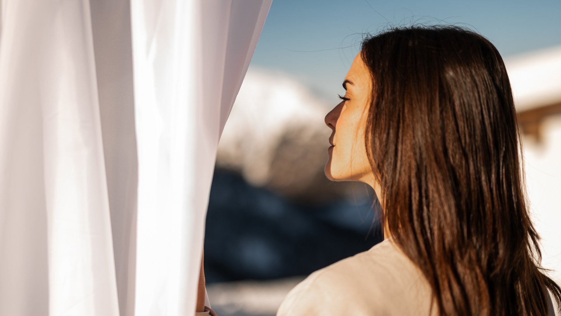 ADEA Lifestyle Suites – romantisches Hotel in Tirol Frau öffnet weißen Vorhang und schaut nach draußen bei Tageslicht