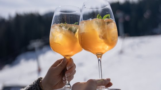 Personen mit zwei Gläser mit eisgekühlten Drinks stoßen im Winter vor der Skipiste an Personen mit zwei Gläser mit eisgekühlten Drinks stoßen im Winter vor der Skipiste an