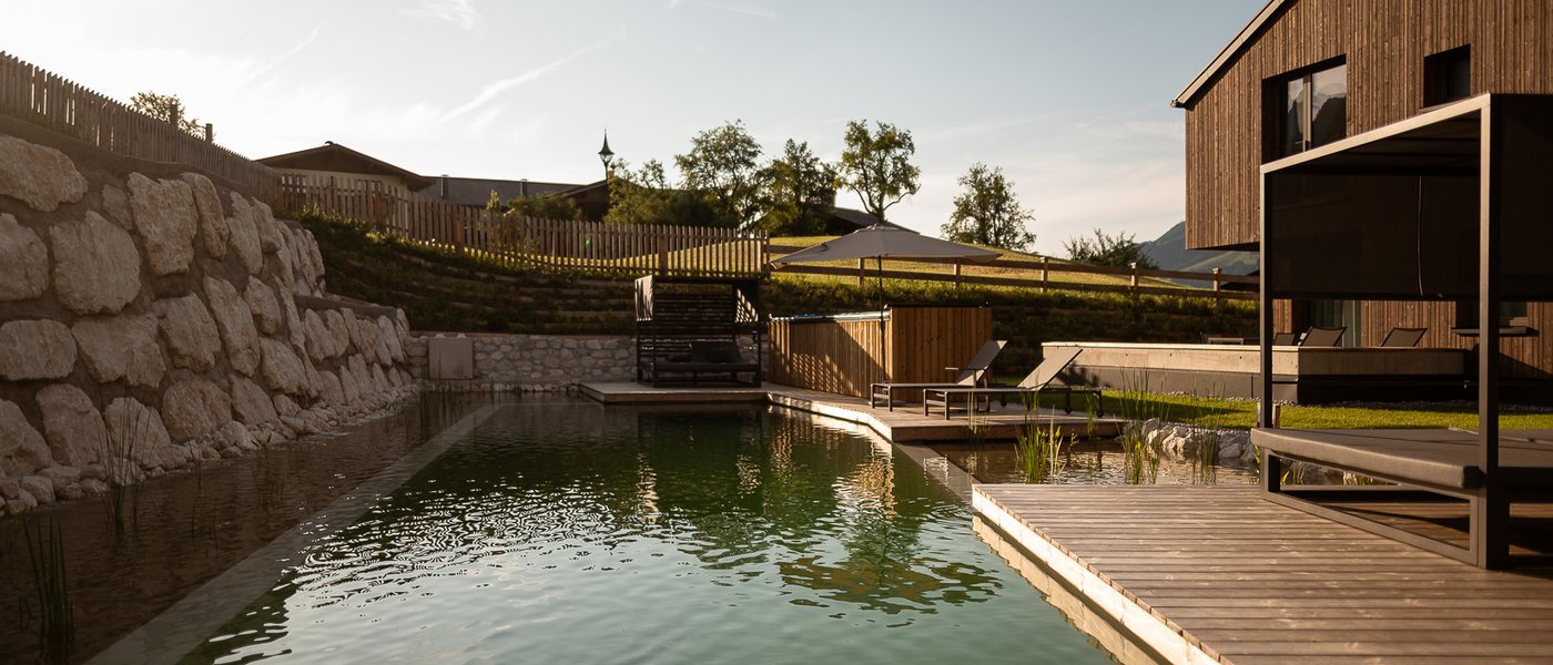 Day Spa inmitten der Kitzbüheler Alpen Moderner Naturpool mit Holzterrasse und Liegestühlen neben einem Holzhaus