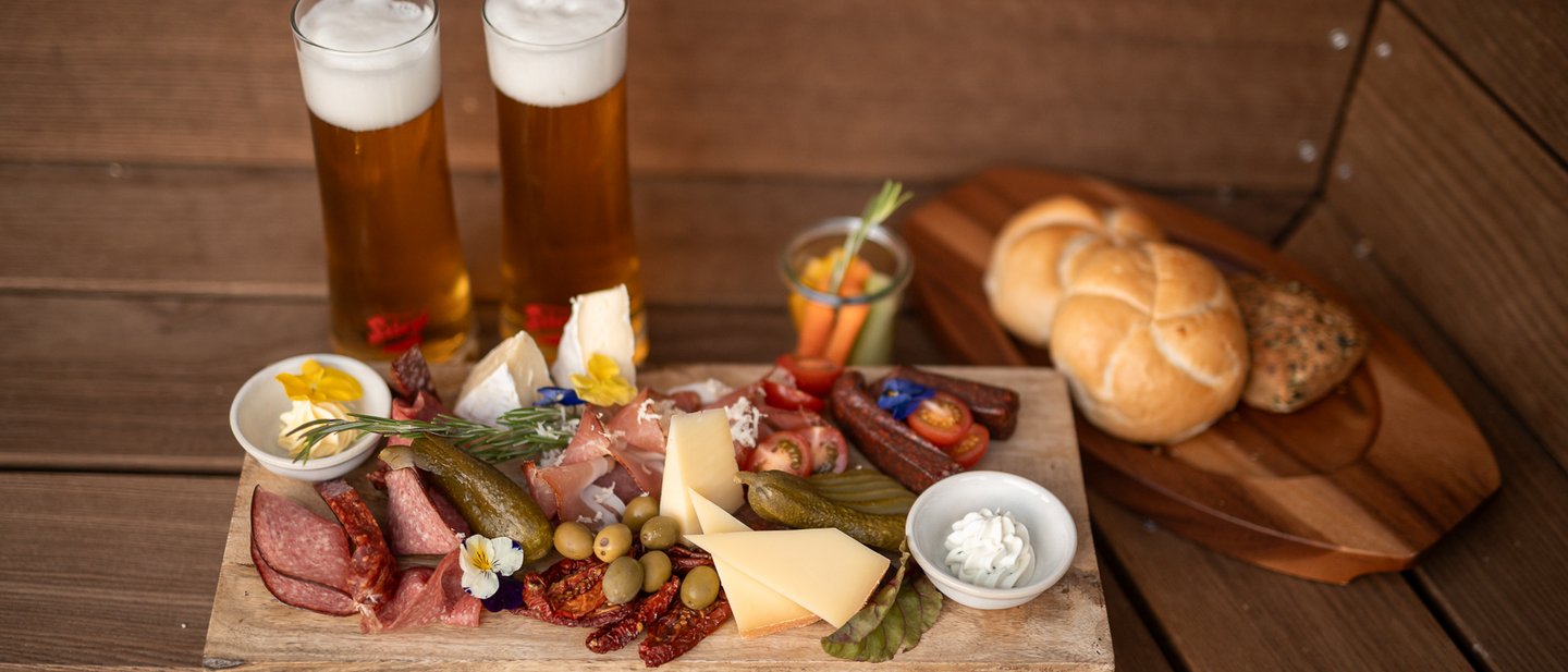 Platter with ham, bacon, cheese, vegetables, bread and two glasses of beer Platter with ham, bacon, cheese, vegetables, bread and two glasses of beer