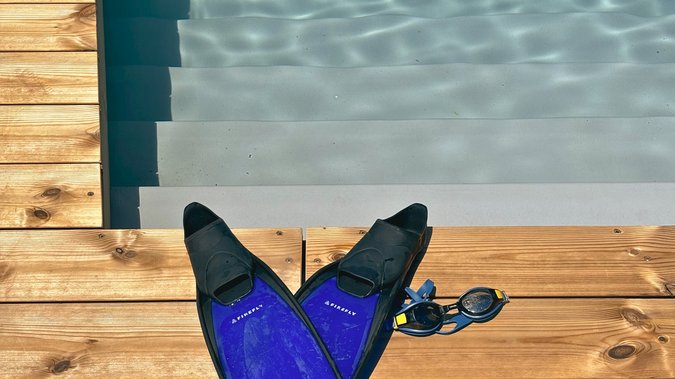 Blue swimming fins and goggles are lying on the jetty in front of the swimming pond. Blue swimming fins and goggles are lying on the jetty in front of the swimming pond.