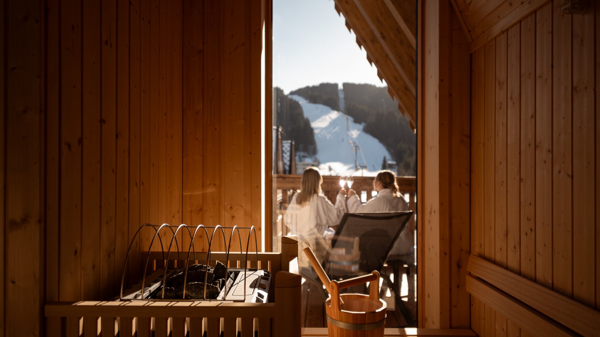 Hotel in Fieberbrunn: ADEA Lifestyle Suites Sauna mit Blick auf verschneite Berge und zwei Personen auf dem Balkon