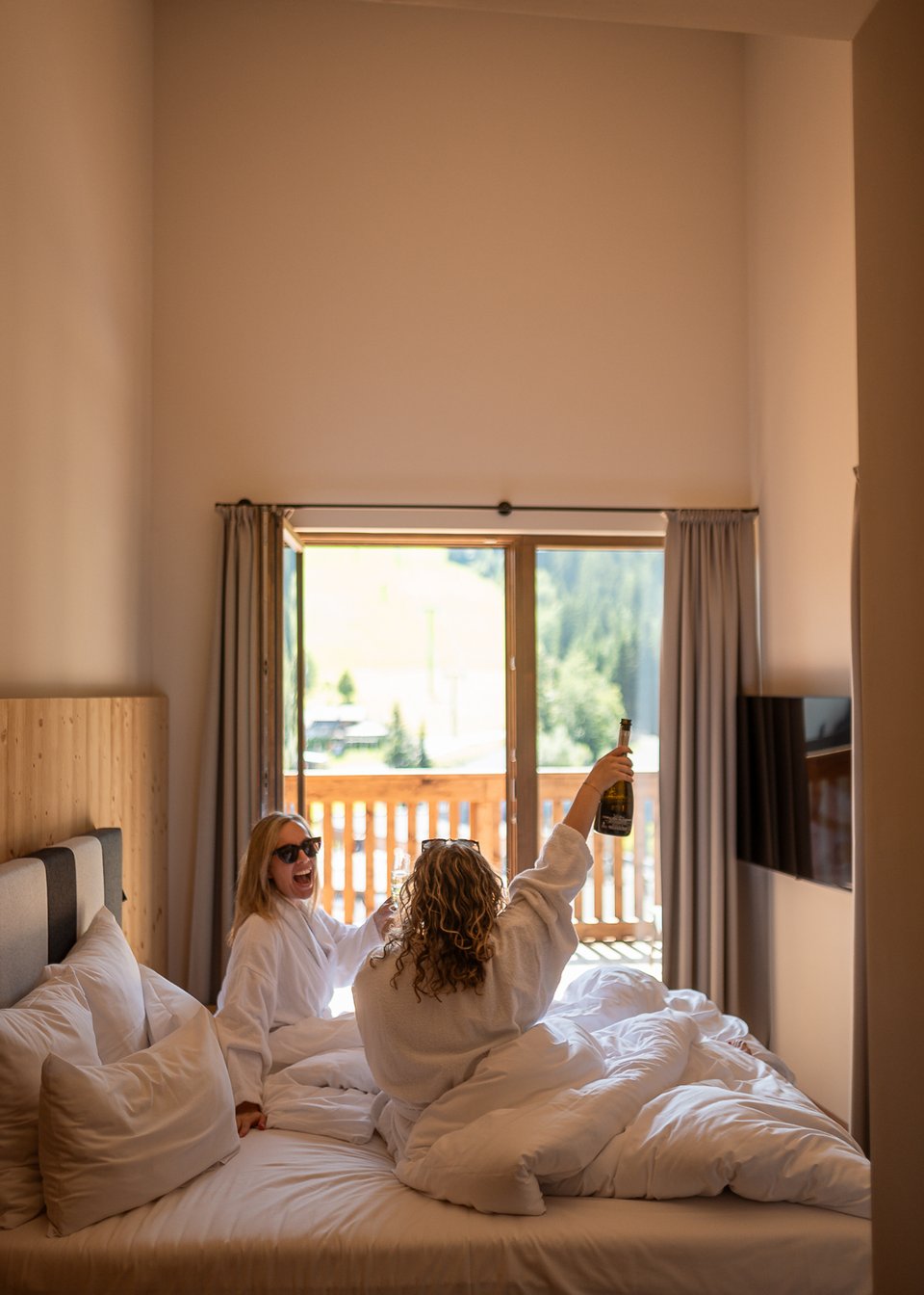 ADEA Lifestyle Suites: Unterkunft in Fieberbrunn Zwei Frauen feiern im Hotelzimmer mit Champagner und genießen die Aussicht vom Balkon