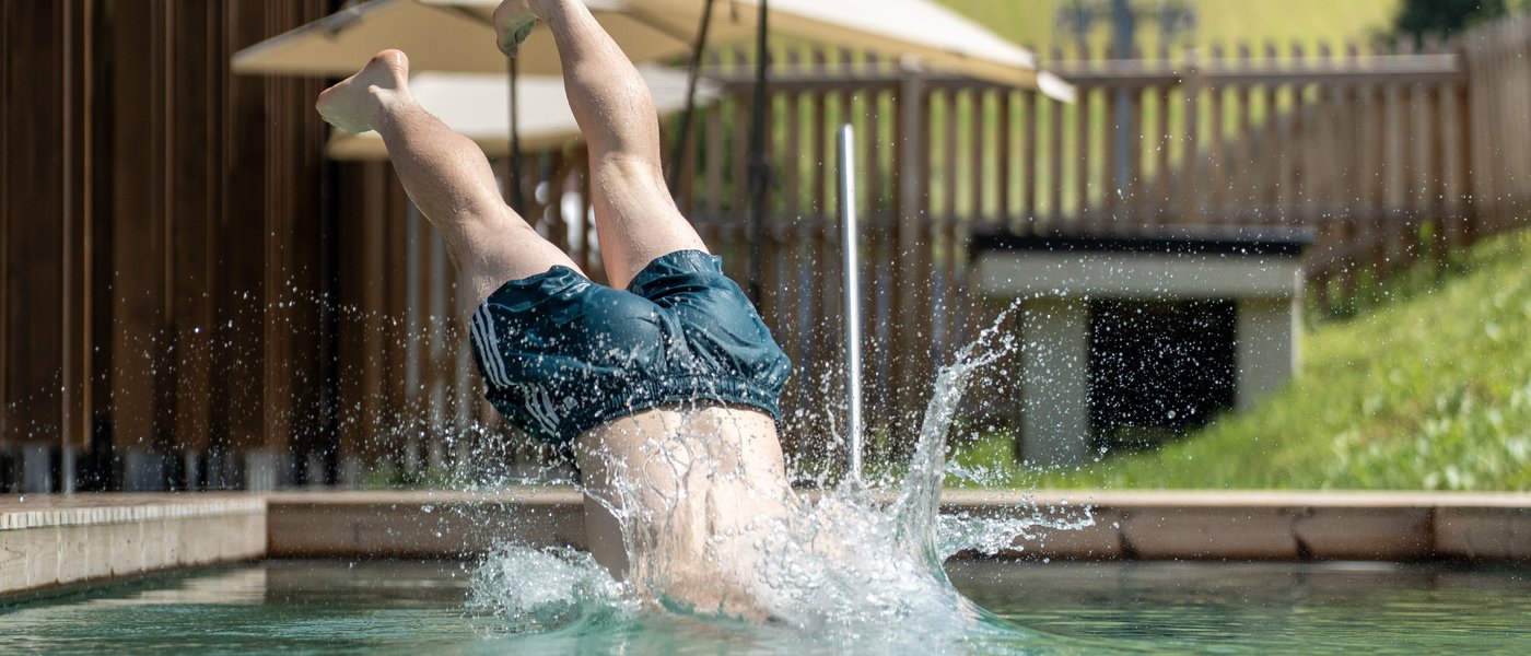 Hotel in Fieberbrunn: the ADEA Lifestyle Suites Person diving headfirst into a pool with grassy hillside in background