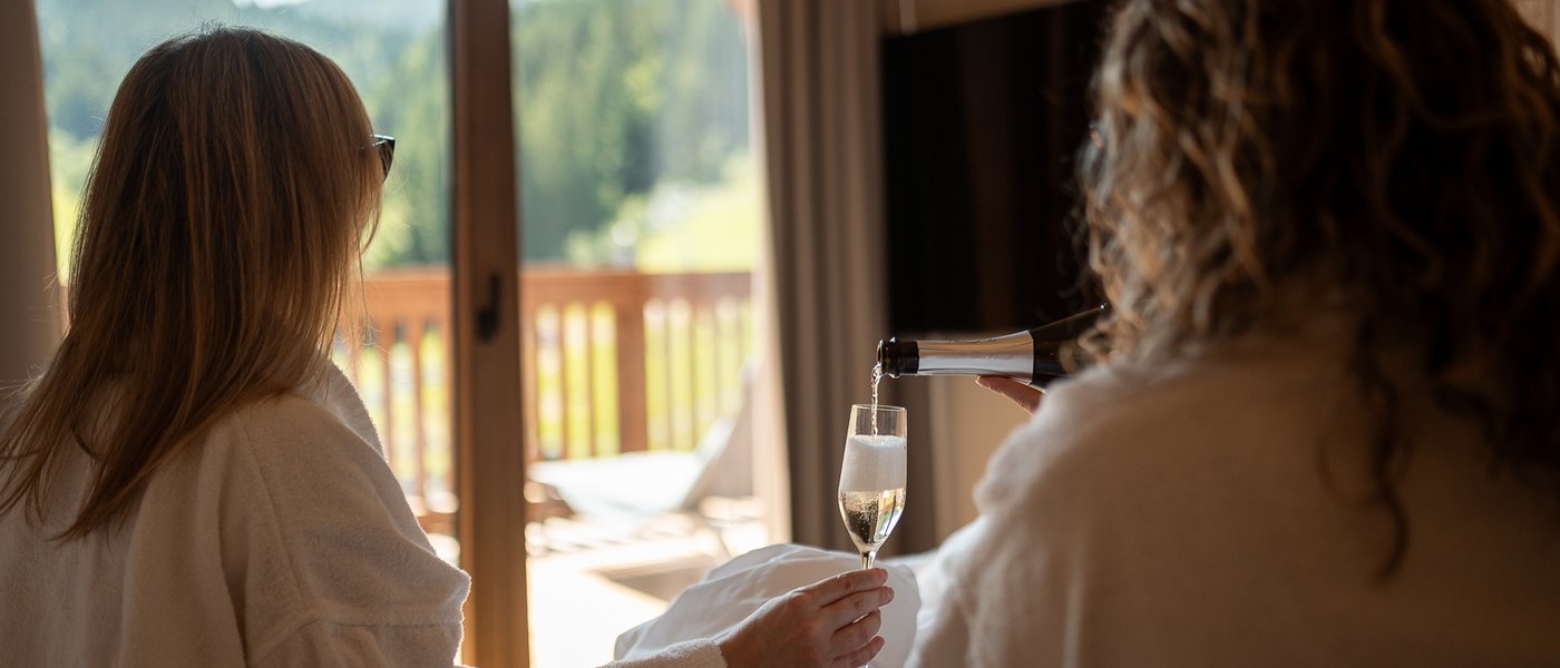 Mit Freundinnen in den Urlaub in Österreich Zwei Frauen in Bademänteln genießen Sekt auf einem Balkon mit Bergblick