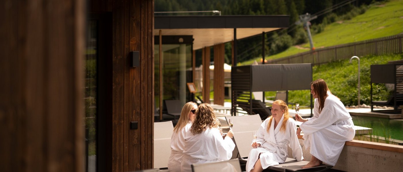 Mit Freundinnen in den Urlaub in Österreich Vier Frauen in Bademänteln sitzen draußen auf Liegestühlen und stoßen an