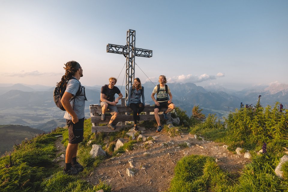 UpsideDown Restaurant Four hikers on mountain summit next to large summit cross at sunset